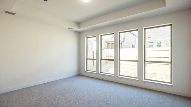 carpeted spare room with a tray ceiling, visible vents, and baseboards