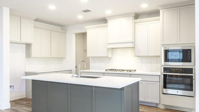 kitchen featuring an island with sink, stainless steel appliances, a sink, and light countertops