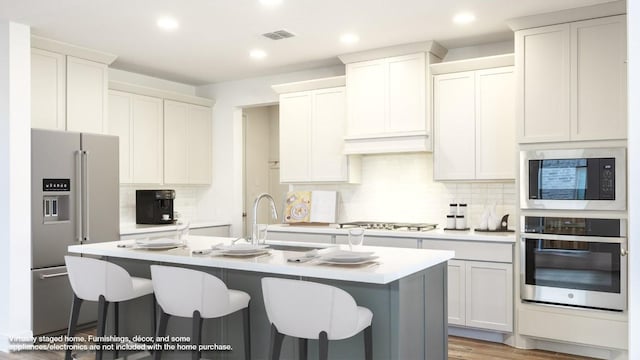 kitchen featuring appliances with stainless steel finishes, light countertops, visible vents, and an island with sink