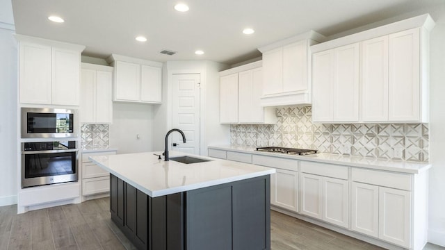 kitchen with appliances with stainless steel finishes, a sink, light wood-style flooring, tasteful backsplash, and recessed lighting