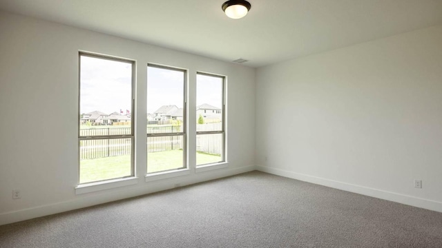 carpeted empty room featuring plenty of natural light, baseboards, and a residential view