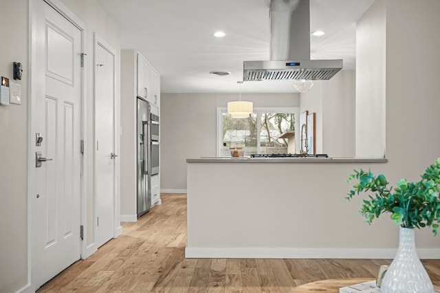 kitchen featuring kitchen peninsula, light hardwood / wood-style flooring, decorative light fixtures, island range hood, and white cabinetry