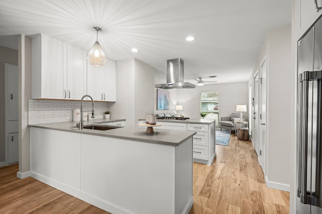 kitchen with kitchen peninsula, wall chimney exhaust hood, stainless steel appliances, sink, and white cabinetry