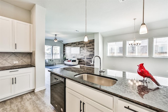 kitchen featuring pendant lighting, ceiling fan with notable chandelier, sink, dark stone countertops, and black dishwasher