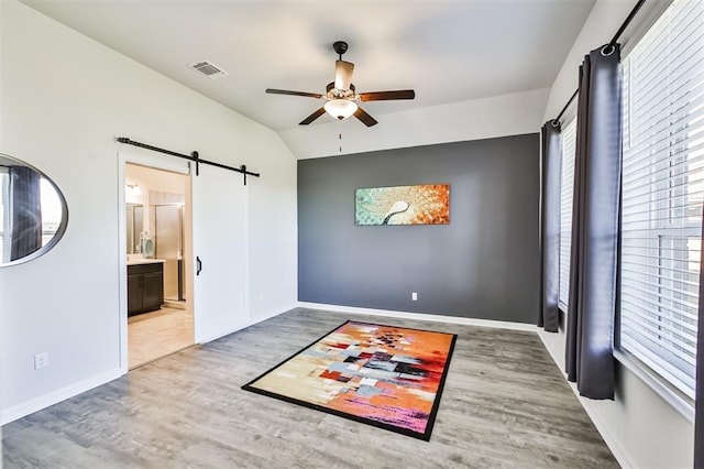 spare room with ceiling fan, a wealth of natural light, a barn door, wood-type flooring, and vaulted ceiling