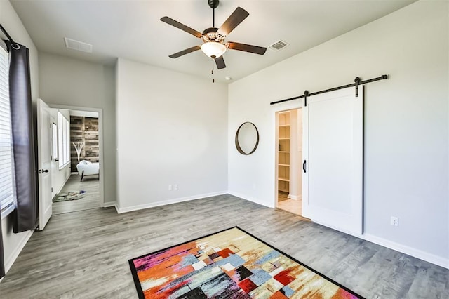 unfurnished bedroom with hardwood / wood-style floors, ceiling fan, a barn door, and multiple windows