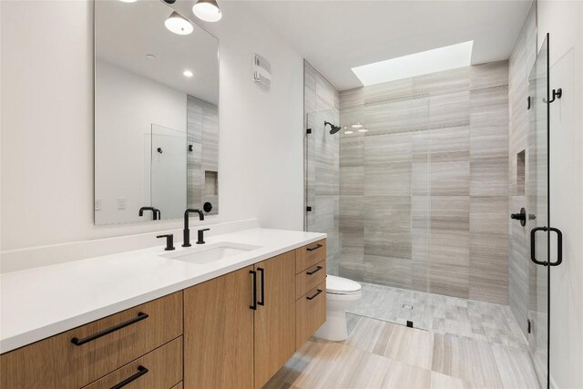 bathroom with a shower with door, a skylight, vanity, and toilet