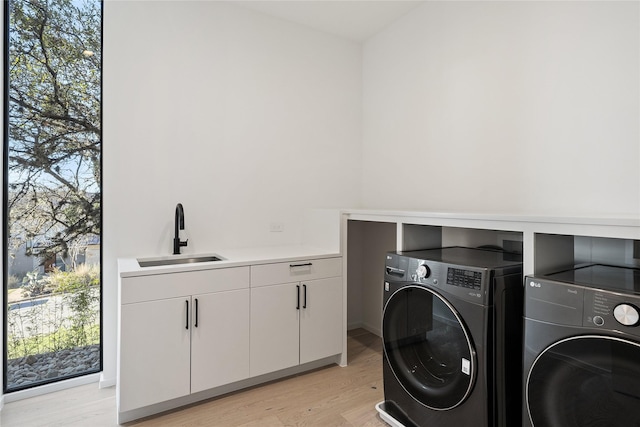 clothes washing area with sink, washer and dryer, cabinets, and light hardwood / wood-style flooring