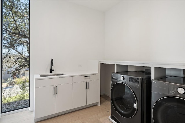 laundry room with washing machine and dryer, a sink, a healthy amount of sunlight, light wood-style floors, and cabinet space