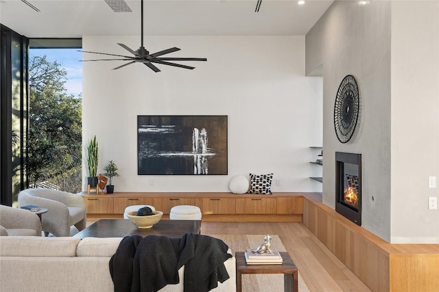 living room with visible vents, a ceiling fan, light wood-style floors, a wall of windows, and a glass covered fireplace