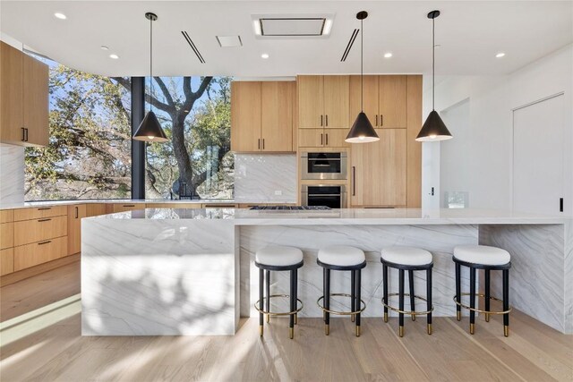 kitchen featuring decorative light fixtures, a large island, light brown cabinets, light hardwood / wood-style floors, and light stone countertops