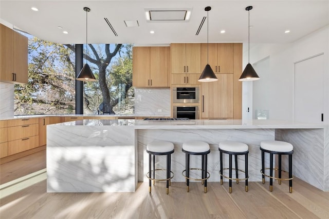 kitchen featuring light stone counters, a kitchen breakfast bar, decorative backsplash, light brown cabinetry, and modern cabinets