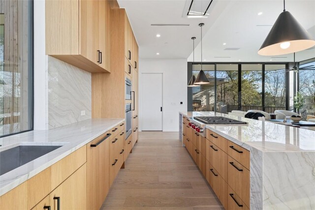 kitchen featuring stainless steel gas cooktop, light stone counters, light brown cabinets, decorative backsplash, and pendant lighting