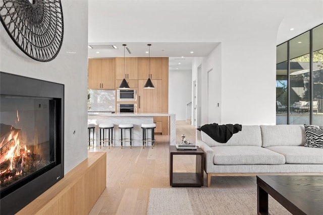 living room with light wood-style floors, recessed lighting, floor to ceiling windows, and a glass covered fireplace