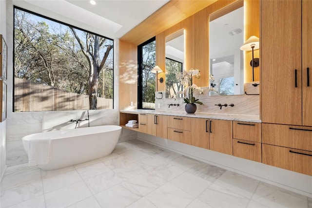 bathroom with marble finish floor, visible vents, a freestanding tub, and double vanity