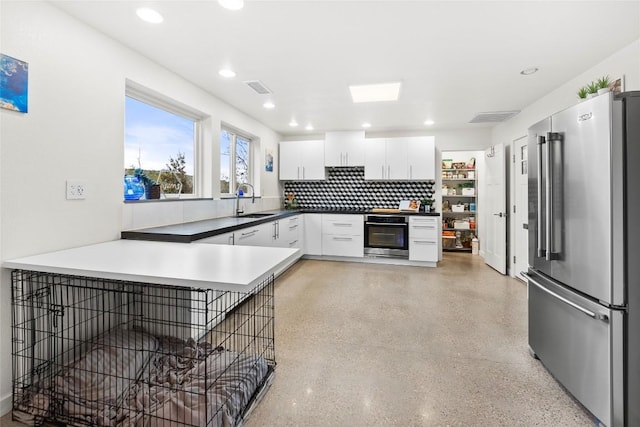 kitchen with kitchen peninsula, backsplash, stainless steel appliances, sink, and white cabinetry