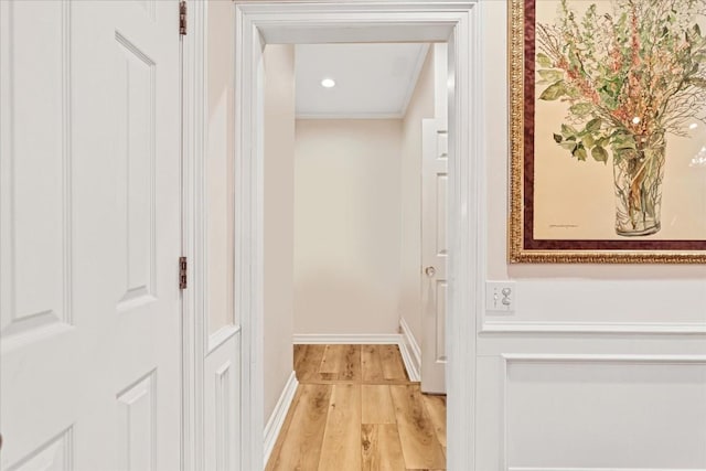 corridor with ornamental molding and light hardwood / wood-style flooring