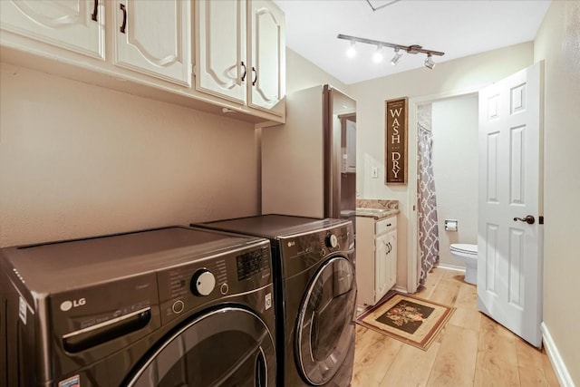 clothes washing area featuring washing machine and clothes dryer, cabinets, track lighting, and light wood-type flooring