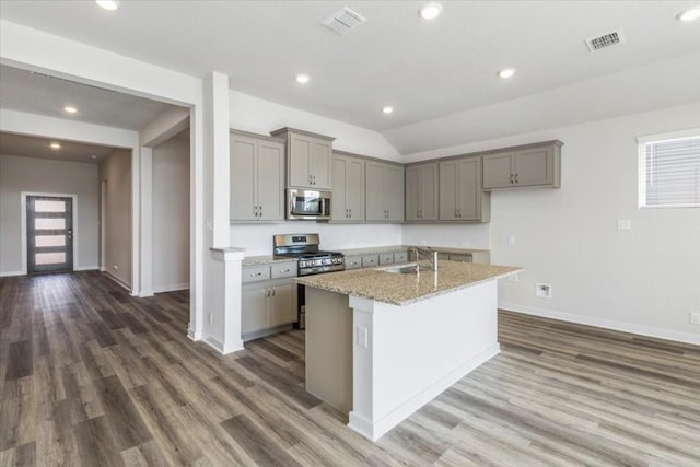 kitchen with gray cabinetry, light stone counters, stainless steel appliances, and an island with sink