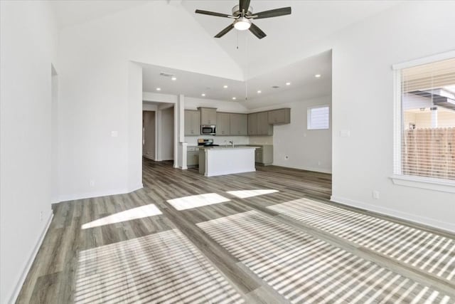 unfurnished living room featuring hardwood / wood-style floors, high vaulted ceiling, ceiling fan, and a healthy amount of sunlight