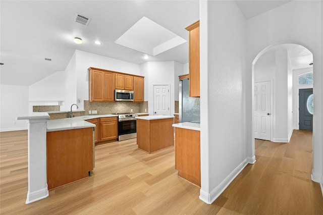 kitchen featuring appliances with stainless steel finishes, backsplash, a center island, light hardwood / wood-style floors, and kitchen peninsula