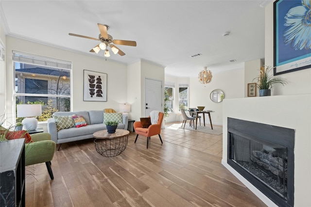 living room with wood-type flooring, ceiling fan with notable chandelier, and crown molding