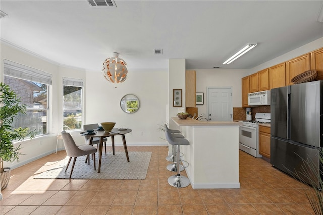 kitchen featuring a breakfast bar, white appliances, backsplash, and light tile patterned floors