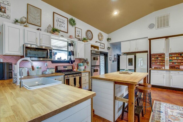 kitchen featuring white cabinets, stainless steel appliances, tasteful backsplash, and lofted ceiling