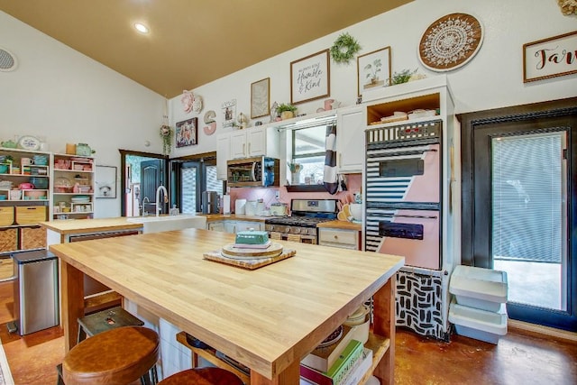 kitchen with kitchen peninsula, stainless steel appliances, sink, high vaulted ceiling, and white cabinetry