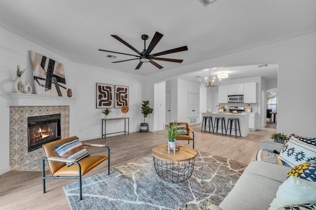 living room featuring a fireplace, light hardwood / wood-style floors, ceiling fan with notable chandelier, and ornamental molding