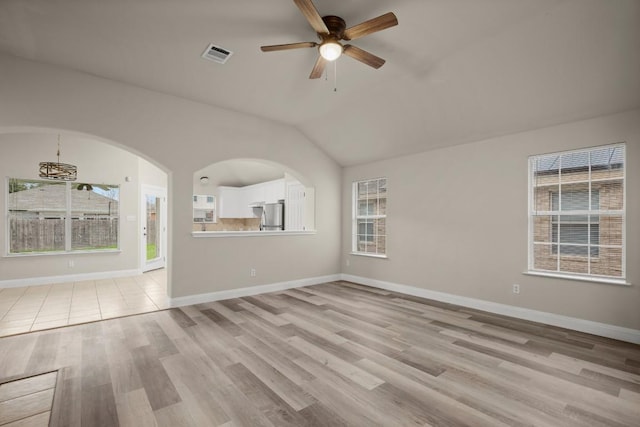 unfurnished living room featuring vaulted ceiling, light hardwood / wood-style flooring, a healthy amount of sunlight, and ceiling fan with notable chandelier