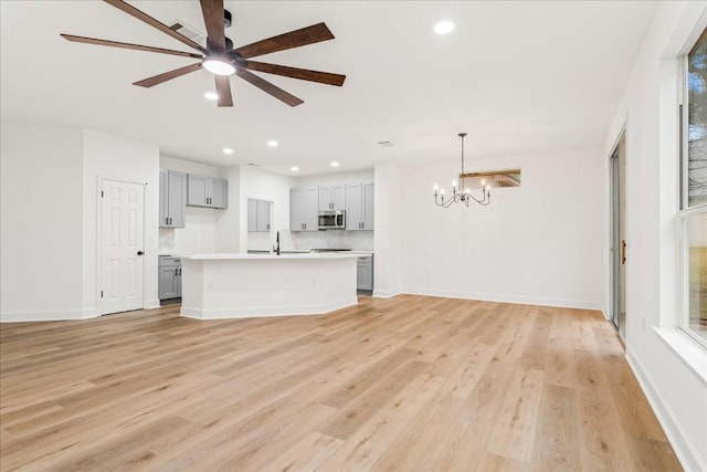 unfurnished living room featuring sink, light hardwood / wood-style floors, and ceiling fan with notable chandelier