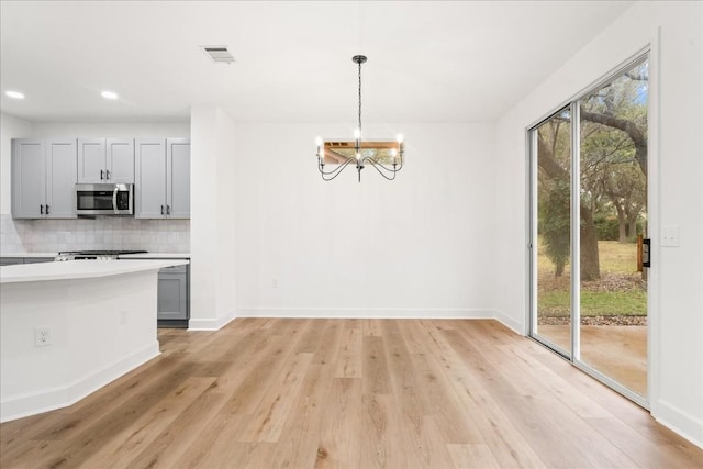 kitchen featuring tasteful backsplash, pendant lighting, light hardwood / wood-style flooring, a chandelier, and gray cabinets