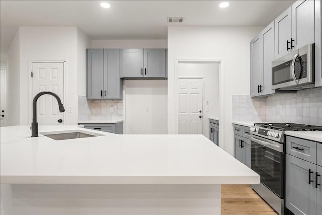 kitchen featuring an island with sink, stainless steel appliances, gray cabinets, and sink