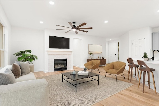 living room with ceiling fan, light hardwood / wood-style floors, and a tiled fireplace