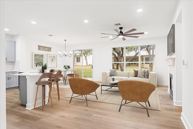 living room with ceiling fan with notable chandelier, light hardwood / wood-style floors, and sink