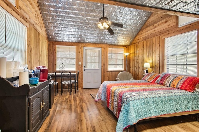 bedroom with wood-type flooring, vaulted ceiling, ceiling fan, and wooden walls