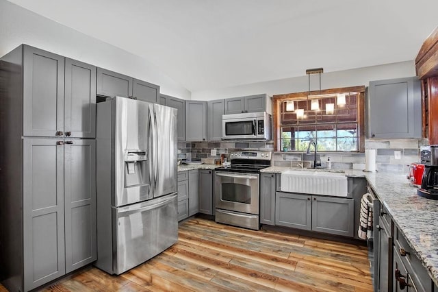 kitchen with sink, vaulted ceiling, decorative backsplash, gray cabinets, and appliances with stainless steel finishes