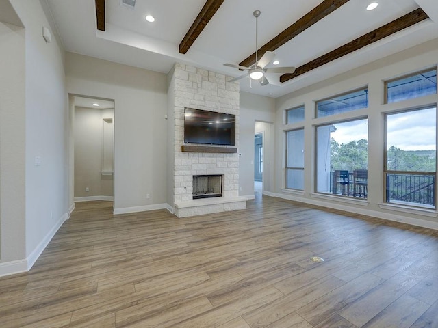 unfurnished living room with beamed ceiling, ceiling fan, a stone fireplace, and light hardwood / wood-style flooring