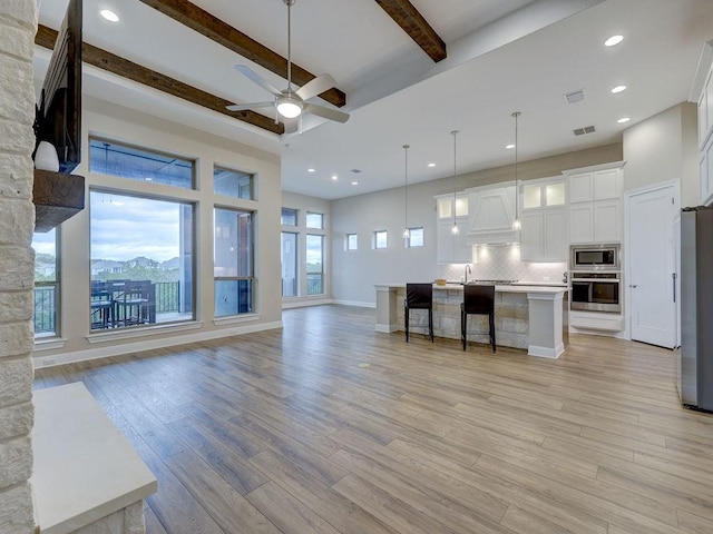 kitchen with beam ceiling, pendant lighting, a center island with sink, white cabinets, and appliances with stainless steel finishes