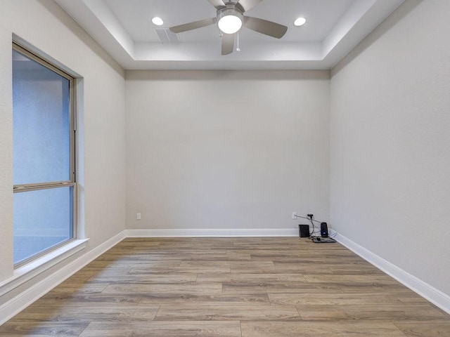 empty room featuring a tray ceiling, ceiling fan, and light hardwood / wood-style flooring