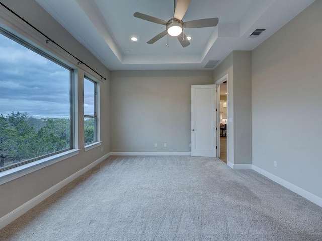 spare room featuring a tray ceiling, ceiling fan, and light colored carpet