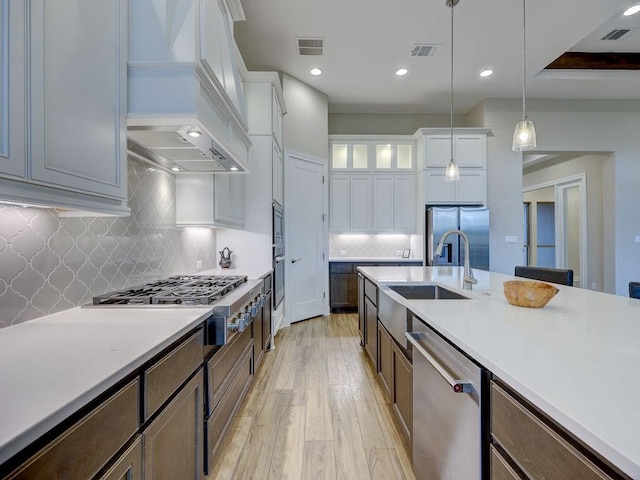 kitchen with decorative backsplash, custom range hood, decorative light fixtures, white cabinetry, and stainless steel appliances