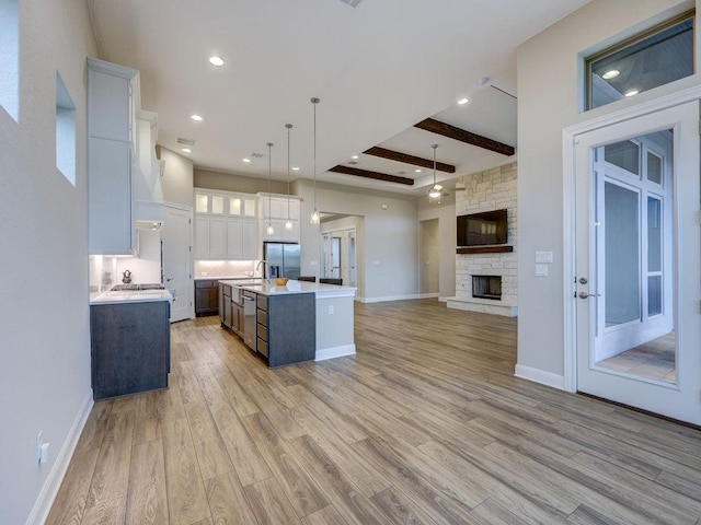 kitchen featuring stainless steel appliances, beam ceiling, decorative light fixtures, a center island with sink, and white cabinetry