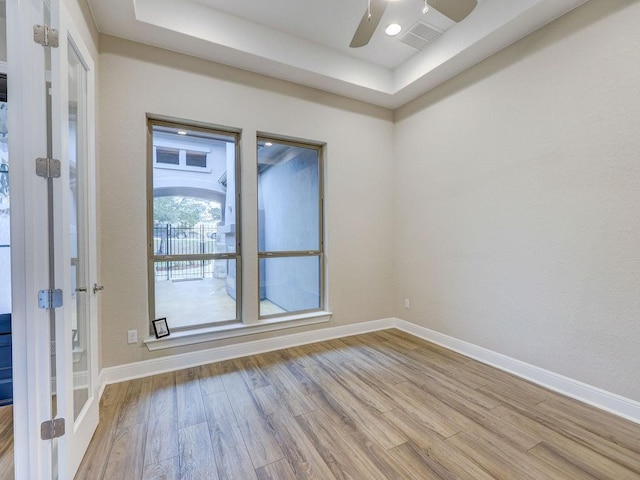 spare room featuring a tray ceiling, ceiling fan, and light hardwood / wood-style flooring