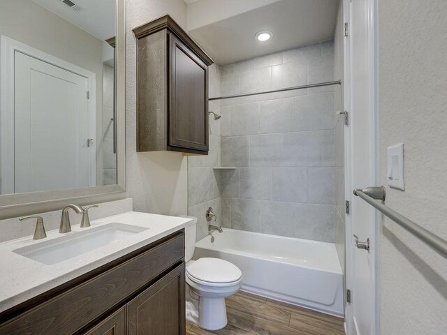 full bathroom featuring hardwood / wood-style floors, tiled shower / bath combo, toilet, and vanity