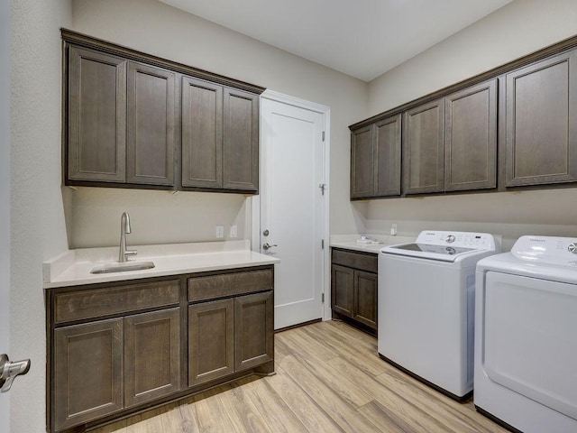 clothes washing area with cabinets, light wood-type flooring, sink, and washing machine and clothes dryer