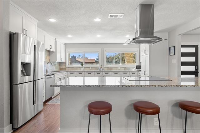 kitchen featuring light stone countertops, a textured ceiling, stainless steel appliances, white cabinetry, and range hood