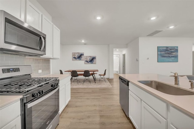 kitchen with sink, stainless steel appliances, tasteful backsplash, light hardwood / wood-style floors, and white cabinets