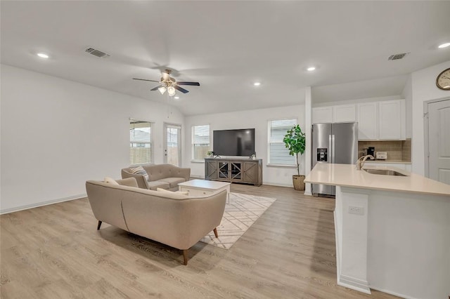 living room featuring ceiling fan, sink, light hardwood / wood-style floors, and vaulted ceiling